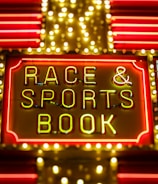 Bright neon lights on a marquee sign display the words 'RACE & SPORTS BOOK'. The sign is surrounded by rows of yellow and white lights against a red background, evoking a vibrant, energetic atmosphere typically associated with casinos or entertainment venues.